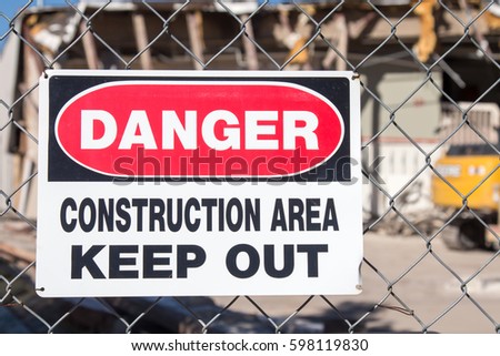 Danger Construction Area sign on a chain link fence in front of a building demolition