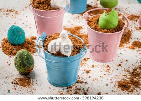 Funny baby food for easter, decorating table. Dessert of chocolate cookies in colored decorative buckets, with colorful chocolate eggs and marshmallow bunnies diving into holes. copy space