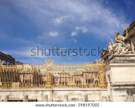 Gold entrance gates to the Palace of Versailles near Paris, France.Deep blue sky, gold gate shimmers in the sun. Stone statue of La Paix (the Peace) by Tuby, woman holding a caduceus with small child.