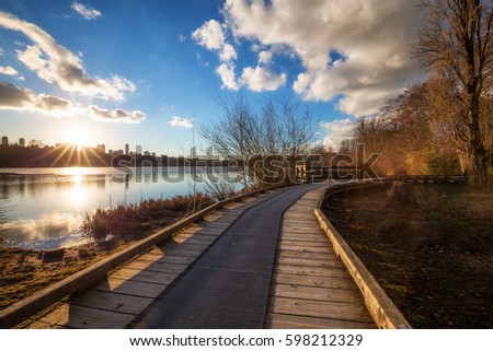 Sunset view on a wooden path in Deer Lake with Metrotown City in the Background. Picture taken in Vancouver, British Columbia, Canada, during a cloudy winter evening.