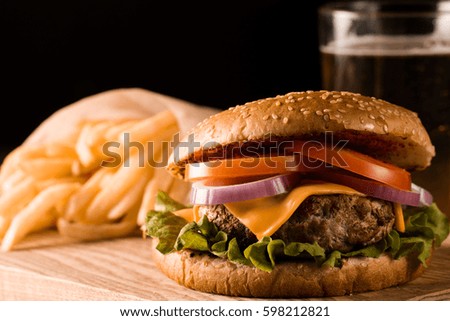 Home made hamburger with beef, onion, tomato, lettuce and cheese. Fresh burger closeup on wooden rustic table with potato fries, beer and chips. Cheeseburger.