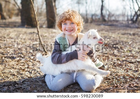 boy and his friend kid on spring farm, white boy with blond curly hair, friendship with little white goat, fall or autumn background, smiling face, early morning, sunny day, time for milk
