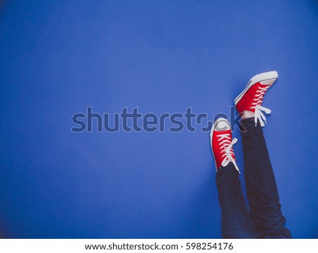 Young man in jeans and red sneakers with his feet against the blue wall.
