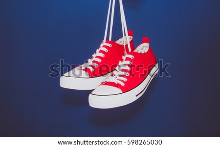 Pair of red sneakers hanging on the laces with blue wall in the background.