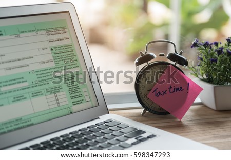 tax time post-it on alarm clock and Individual income tax return form online. Royalty-Free Stock Photo #598347293