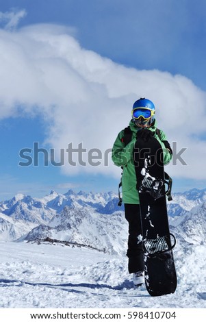 snowboarder standing with snowboard in the mountains. Beautiful winter landscape with ridge, blue sky in the background. Photo on a theme of extreme sports, winter sports, snowboarding. 