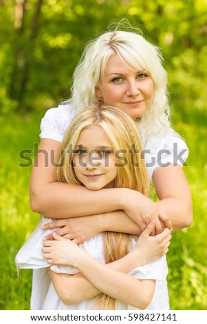 Mom and daughters play in the park in the summer. Blonds posing outdoors