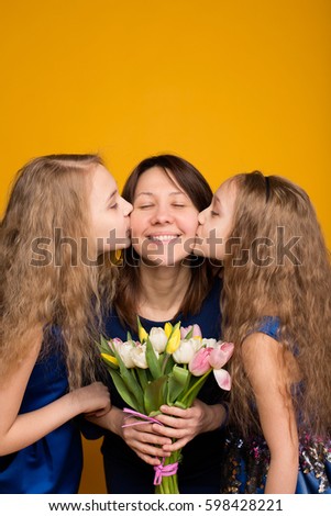 Daughters wish mom a happy holiday bouquet of tulips. Mom and daughter on a yellow background in the studio