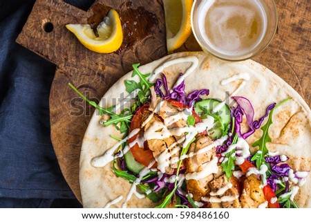 Chicken kebab with vegetables in pita bread and a glass of beer with lemon on a wooden tray.Close up. View from above. 