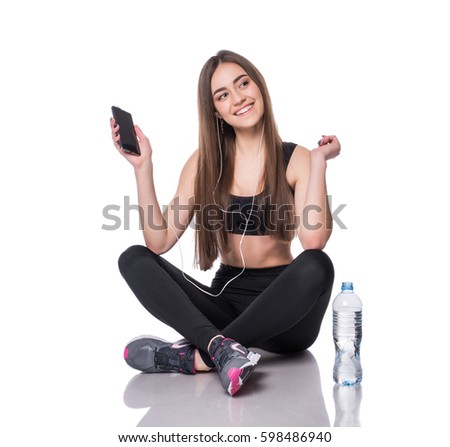 Portrait of a young athlete woman listening to music with earphones over white background. Attractive fitness girl chatting on smartphone ion studio