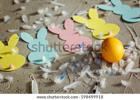 Yellow egg and Garland with colorful paper rabbits and feathers on concrete background. Concept Easter Bunny Banner. Top view.