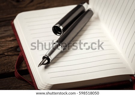 Opened blank notebook with elegant fountain pen on wooden background.