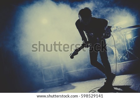 Silhouette of guitar player / guitarist perform on concert stage. Dark background, smoke, concert  spotlights Royalty-Free Stock Photo #598529141