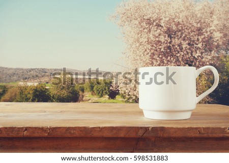 Cup of coffee a wooden table in front of spring landscape background. vintage filtered