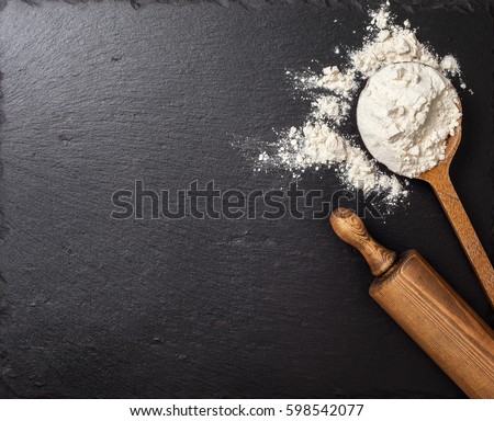  wooden spoon with flour, a rolling pin on a black slate background. Top view, selective focus Royalty-Free Stock Photo #598542077