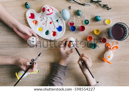 Mother and their daughter hands painting Easter eggs on the wooden background.