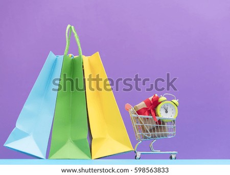 cute small gifts and alarm clock in the cool shopping cart and shopping bags on the wonderful purple background