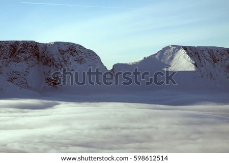 Pass in a mountain ridge above the clouds filled the valley. Clear sky and sun above the mountains and fog in the lowlands.
