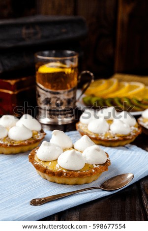 Delicious homemade mini tarts (tartlets) with fruit kiwi and lemon kurd cream with meringue. Served with clear tea mug in cup holder and fruits slices. Tasty sweet small dessert and cake. Vertical. 