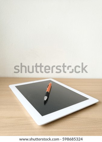 Tablet and pen on wooden table.