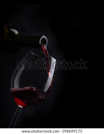 Red wine pouring in wineglass from bottle over black background. Wine list design menu with copyspace. Alcohol beverage card backdrop.
