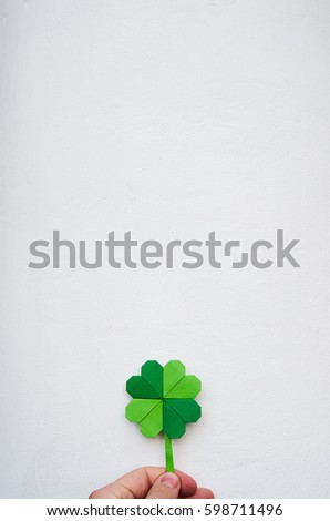 Hand holding paper origami green shamrock on white wall background. Space for copy, lettering, text. St. Patrick's day vertical postcard template.