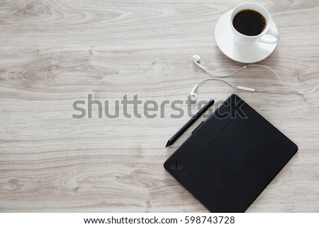 Workplace. On the wooden table there is a graphics tablet, stylus, headphones and white cup of coffee.