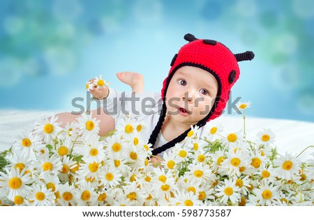 Cute baby lying in the bed on white blanket in ladybug hat. Little boy with chamomille flowers