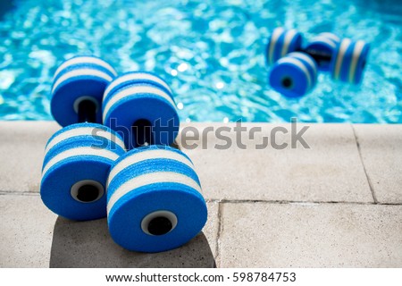 Sportive equipment for aqua aerobics. Plastic dumbbells for aqua fitness at swimming pool on summer day outdoors, nobody