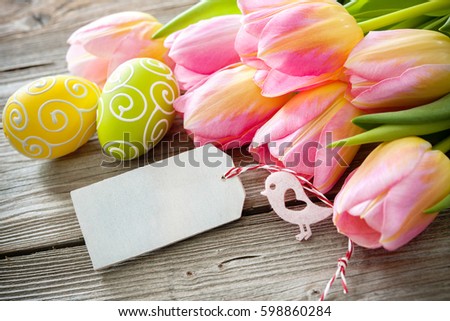 Colorful tulips and easter eggs with an empty tag on wooden background