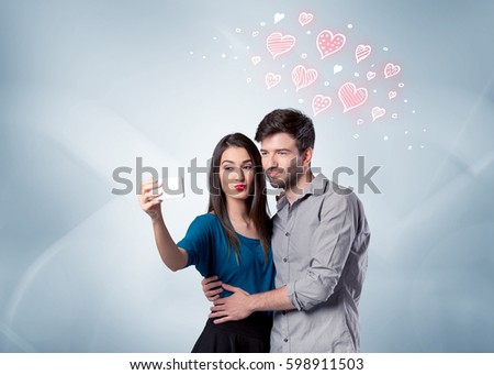 A young couple in love and drawn red hearts taking selfie with a mobile phone in the handsome guy's hand in front of an empty clear grey wall background concept