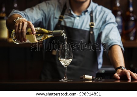 Male sommelier pouring white wine into long-stemmed wineglasses. Royalty-Free Stock Photo #598914851