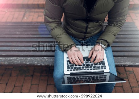 Laptop in a man's hands sitting on a wooden chair. Photo with lens flare filter effect.