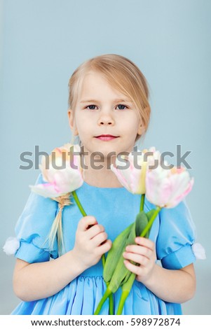 A five-year-old girl holds a bouquet of tulips in her hands. Flowers for mom as a gift. Look at the photo camera
