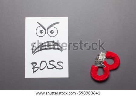  Evil painted boss face with red handcuffs on a white paper  isolated gray background.Sexual harassment concept. Royalty-Free Stock Photo #598980641