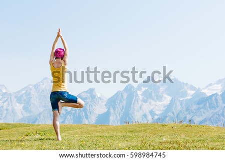 Young woman in yoga pose standing on the grass high in the mountains