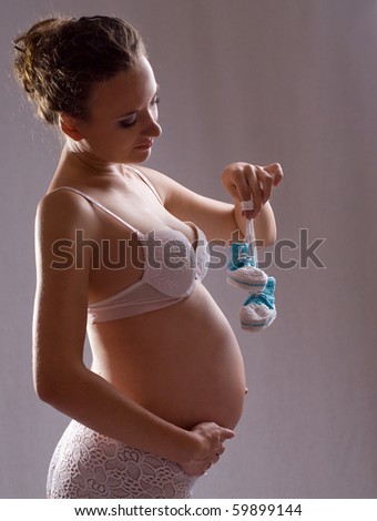 The young beautiful pregnant woman in underwear, holds blue bootees