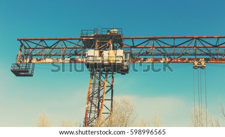 Old, rusty gantry crane on railroad, an abandoned concrete plant. Crisis, collapse of economy, and shutdown of production capacities have led to collapse. Effect of an old vintage photo.