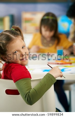 Portrait of happy elementary age child sitting at desk looking at camera in art class in primary school classroom, smiling.?