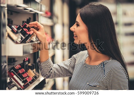 Beautiful girl is choosing lipstick while doing shopping in the mall