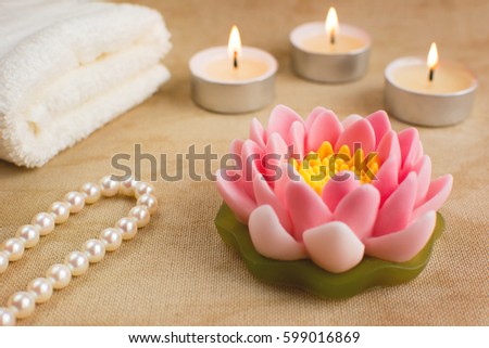 Beautiful handmade soap shaped like lotus flower. Burning candles, string of pearls and towel on the background. Spa concept.
