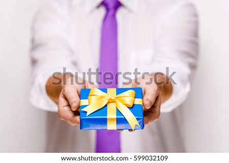 Male hands holding a gift box. Present wrapped with ribbon and bow. Christmas or birthday blue package. Man in white shirt and necktie.