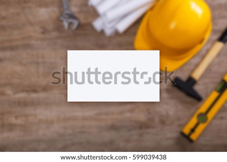 Business card mockup. Adjustable wrench, hammer and building level. Paper plans and helmet. Wood rustic background.