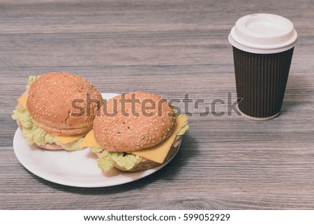 Close up photo of tasty fresh two cheeseburgers on a plate and paper cup of hot coffee on grey background