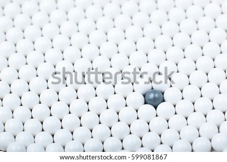 Black bulb among many white ones. Background of airsoft balls.