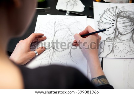 Girl tattoo artist draws a sketch with a sheet of Monstera. Close-up of hand drawing with a creative workplace