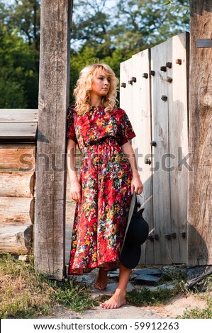 Beautiful young blond woman in rural area standing in the wooden gate barefoot