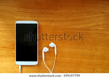 technology, music, gadget and object concept - close up of white smartphone and earphones on wooden surface