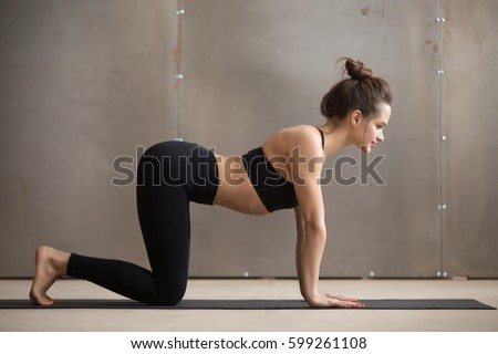 Young attractive woman in black practicing yoga, standing in asana paired with Cat Pose on the exhale, Cow exercise, Bitilasana pose, working out, cool urban style, full length, grey studio background