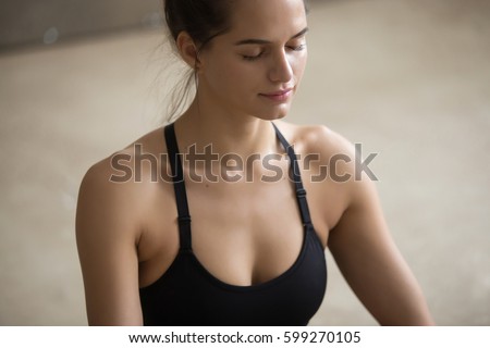 Portrait of young calm yogi woman practicing yoga, sitting and meditating with closed eyes, relaxing and working out, wearing black sportswear, cool urban style, closeup, grey studio background  Royalty-Free Stock Photo #599270105